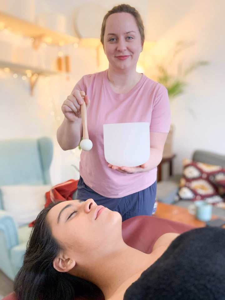 A woman receiving a sound bath with crystal bowls in a cozy, softly lit room